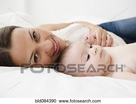 Stock Image - Mother laying on bed with baby. Fotosearch