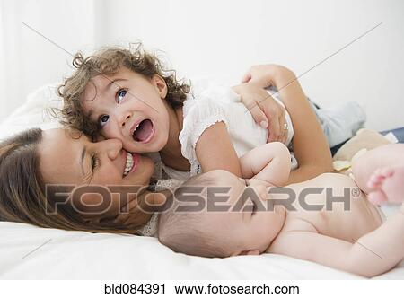 Stock Image - Mother laying on bed with daughters. Fotosearch
