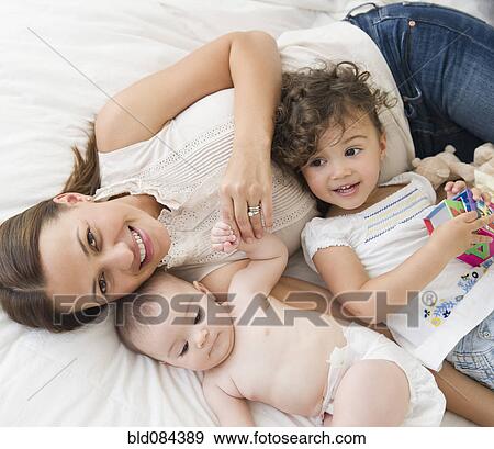 Stock Photo - Mother laying on bed with daughters. Fotosearch