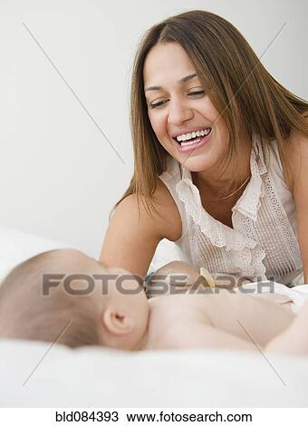 Stock Image - Mother smiling at baby on bed. Fotosearch