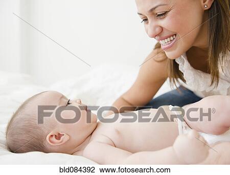 Stock Image - Mother smiling with baby on bed. Fotosearch