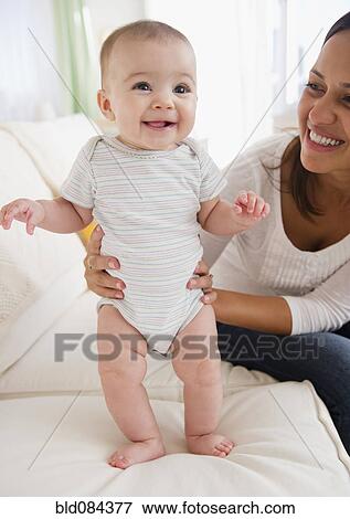 Stock Photo - Mother supporting baby on sofa. Fotosearch