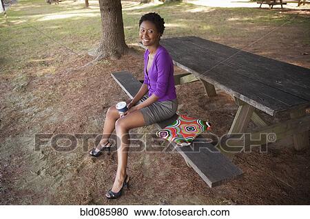Stock Image - African American businesswoman with laptop sitting on picnic bench. Fotosearch