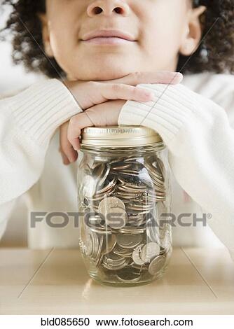 Stock Image - African American girl holding jar of coins. Fotosearch