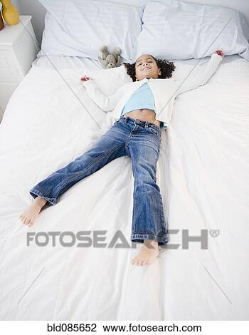 Stock Image - African American girl laying on bed. Fotosearch