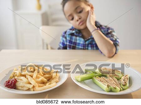 Stock Image - African American girl looking at healthy and unhealthy food. Fotosearch