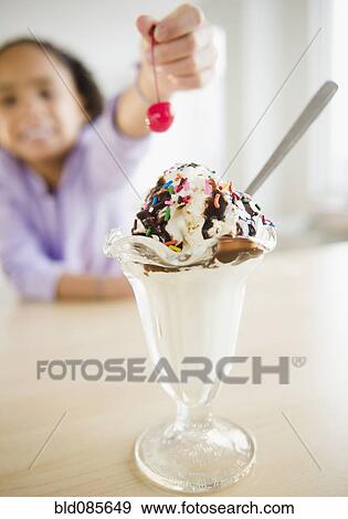Stock Photo - African American girl putting cherry ice cream sundae. Fotosearch
