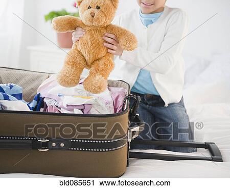 Stock Image - African American girl putting teddy bear in suitcase. Fotosearch