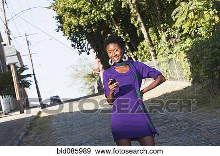 Stock Photo - African American woman text messaging on cell phone outdoors. Fotosearch