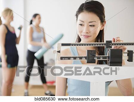 Stock Image - Asian woman weighing herself on scale. Fotosearch