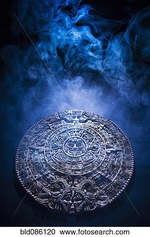Stock Image - Aztec calendar stone carving surrounded by smoke. Fotosearch