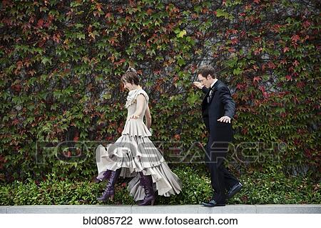 Stock Image - Bride and broom walking on ledge. Fotosearch