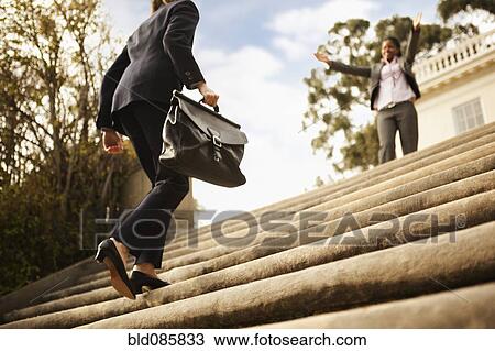 Stock Image - Businesswoman walking up stairs toward co-worker. Fotosearch