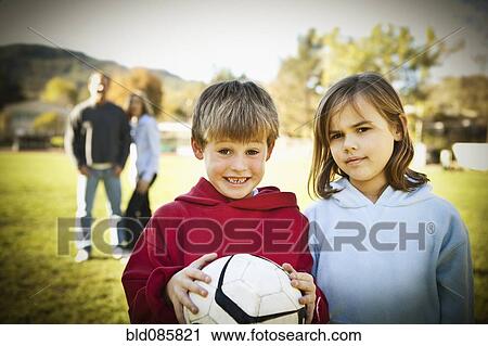 Stock Image - Caucasian boy and girl standing with soccer ball. Fotosearch