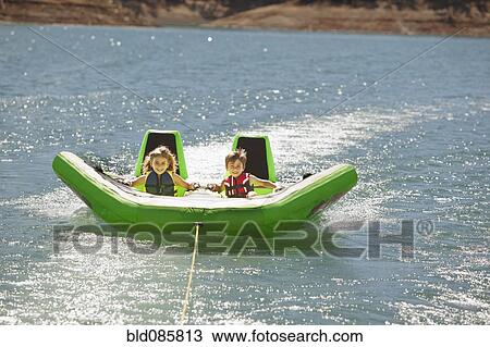 Stock Image - Children riding inflatable raft on lake. Fotosearch