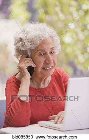 Stock Image - Chilean woman talking on cell phone and using laptop. Fotosearch