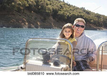 Stock Image - Father and daughter steering boat on lake. Fotosearch