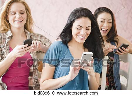 Stock Image - Friends text messaging on cell phones together. Fotosearch