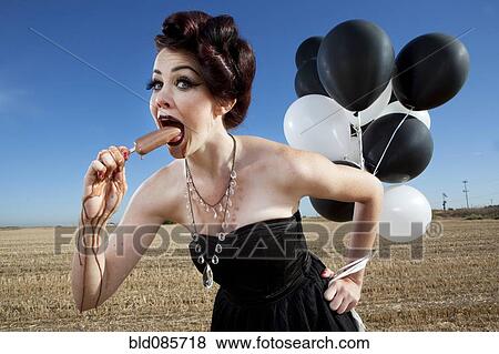 Stock Photo - Glamorous woman holding balloons and eating popsicle. Fotosearch