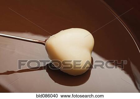 Stock Image - Heart-shaped candy being dipped in chocolate. Fotosearch