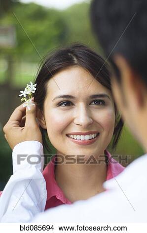 Picture - Hispanic husband putting flower behind wife's ear. Fotosearch