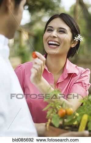 Stock Image - Hispanic woman feeding tomato to husband. Fotosearch