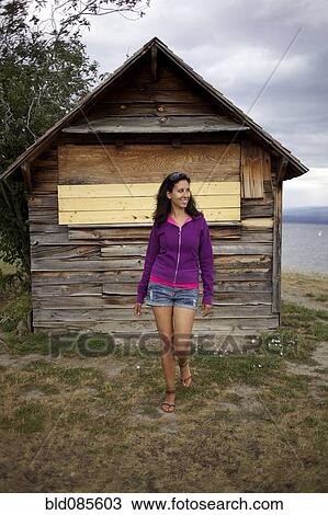 Stock Image - Hispanic woman standing near wooden shed. Fotosearch