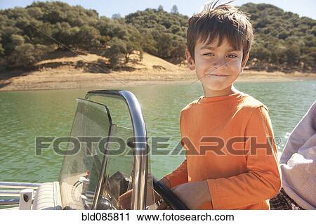 Stock Image - Mixed race boy steering boat on lake. Fotosearch