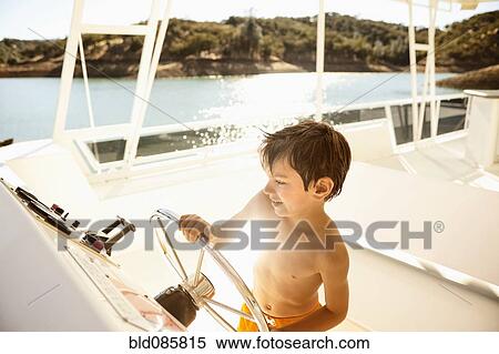Stock Photography - Mixed race boy steering boat on lake. Fotosearch