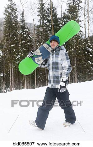 Stock Photo - Mixed race snowboarder carrying snowboard. Fotosearch