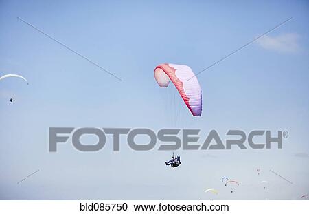 Stock Image - Person paragliding against blue sky. Fotosearch