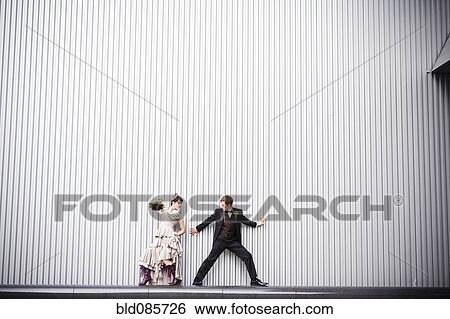 Stock Photograph - Playful bride and groom standing near wall. Fotosearch