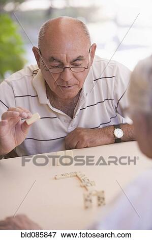 Stock Photo - Senior men playing dominoes outdoors. Fotosearch