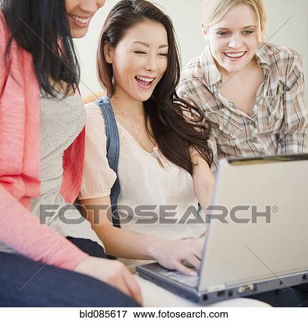 Smiling friends using laptop together View Large Photo Image Stock Photo - Smiling friends using laptop together. Fotosearch