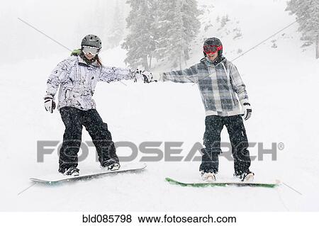 Stock Photo - Snowboarders holding hands on ski slope. Fotosearch