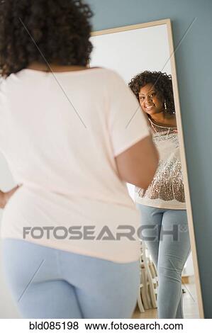 Stock Photo - African American woman looking at reflection in mirror. Fotosearch