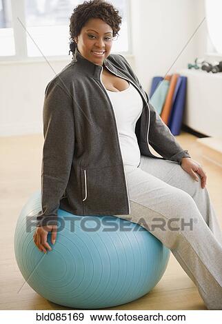 Stock Photo - African American woman sitting on exercise ball. Fotosearch