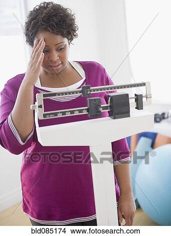 Picture - African American woman weighing herself. Fotosearch