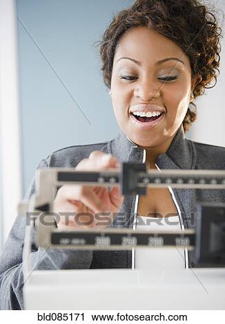 Stock Image - African American woman weighing herself. Fotosearch