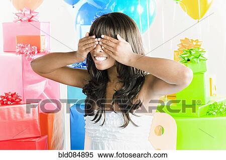 Stock Photography - African American woman with eyes covered next to birthday presents. Fotosearch