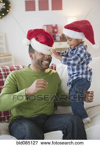 Stock Photo - Black boy putting Santa hat on his father. Fotosearch