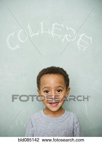 Stock Image - Black boy standing underneath the word college on blackboard. Fotosearch
