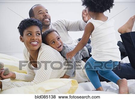 Stock Photo - Black family laying on bed together. Fotosearch