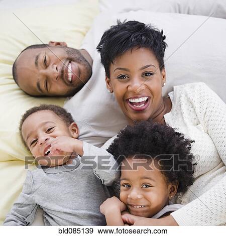 Stock Photo - Black family laying on bed together. Fotosearch