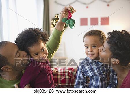 Stock Image - Black father holding mistletoe over daughterís head. Fotosearch