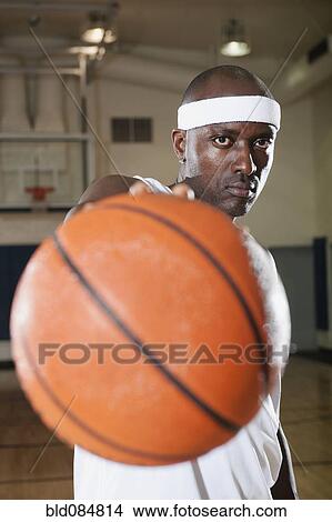 Picture - Black man holding basketball on basketball court. Fotosearch