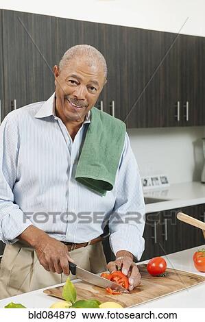 Stock Photo - Black man slicing tomatoes in kitchen. Fotosearch
