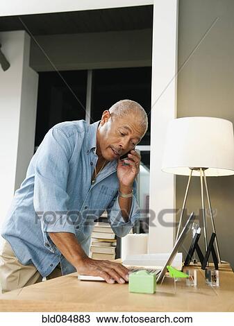 Stock Image - Black man talking on cell phone and using laptop. Fotosearch