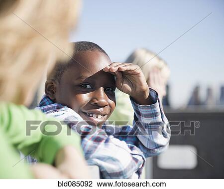 Stock Image - Boy on rooftop with friends shielding eyes. Fotosearch