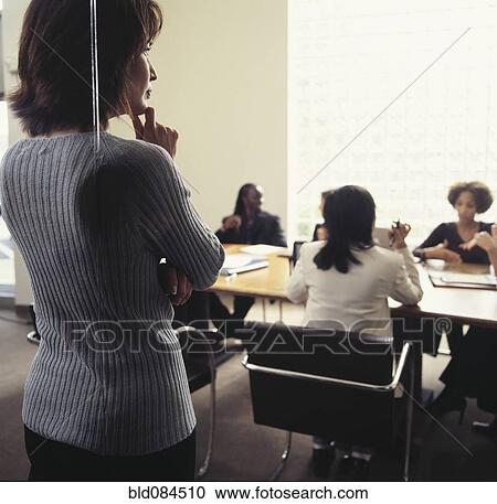 Stock Image - Businesswoman watching co-workers in conference room. Fotosearch